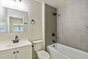 Full bathroom featuring a textured ceiling, vanity, tiled shower / bath combo, and toilet