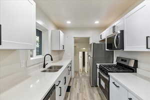 Kitchen featuring light stone counters, stainless steel appliances, sink, light hardwood / wood-style flooring, and white cabinets