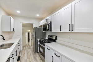 Kitchen with appliances with stainless steel finishes, light wood-type flooring, white cabinetry, and sink