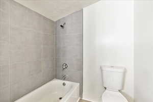 Bathroom featuring a textured ceiling, toilet, and tiled shower / bath