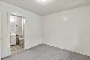 Unfurnished bedroom with ensuite bath and light colored carpet