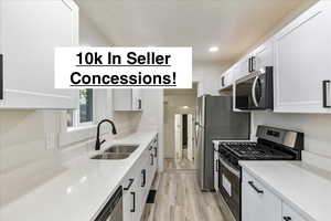 Kitchen with sink, white cabinets, light hardwood / wood-style floors, stainless steel appliances, and light stone countertops