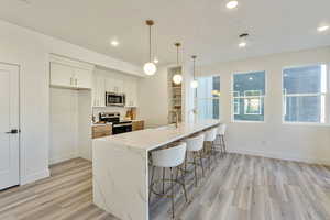 Kitchen featuring light stone countertops, white cabinetry, stainless steel appliances, decorative light fixtures, and light wood-type flooring