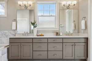 Bathroom with a notable chandelier, vanity, and tiled tub