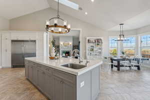 Kitchen with gray cabinetry, a center island with sink, stainless steel built in fridge, hanging light fixtures, and sink