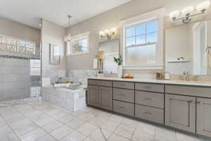 Bathroom featuring a notable chandelier, vanity, plus walk in shower, and a wealth of natural light