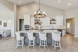 Kitchen featuring a center island with sink, white cabinetry, backsplash, and high vaulted ceiling