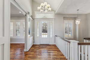 Entrance foyer with a barn door, dark wood-type flooring, a chandelier, and lofted ceiling