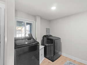 Laundry area with washing machine and dryer, light hardwood / wood-style flooring, and electric panel