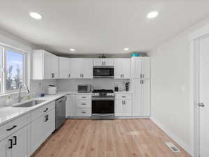 Kitchen with white cabinets, light wood-type flooring, sink, and appliances with stainless steel finishes