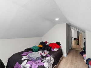 Bedroom with a textured ceiling, light hardwood / wood-style flooring, and lofted ceiling