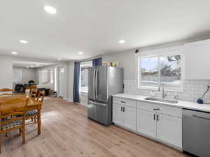 Kitchen with white cabinetry, sink, stainless steel appliances, and light hardwood / wood-style flooring