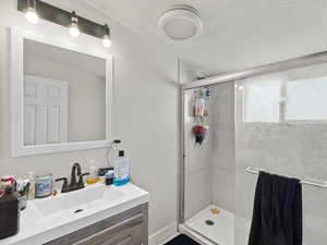 Bathroom featuring a textured ceiling, vanity, and walk in shower