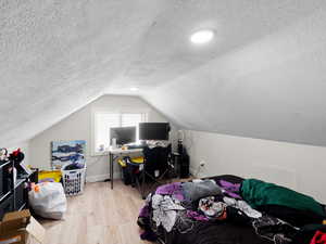 Bedroom with light hardwood / wood-style floors, a textured ceiling, and vaulted ceiling