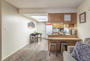 Kitchen featuring sink, light hardwood / wood-style flooring, kitchen peninsula, white appliances, and a breakfast bar area