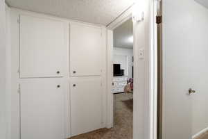 Corridor featuring light colored carpet and a textured ceiling