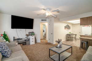 Living room with a textured ceiling, light colored carpet, and ceiling fan