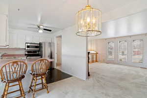 Kitchen with appliances with stainless steel finishes, ceiling fan with notable chandelier, sink, decorative light fixtures, and white cabinets