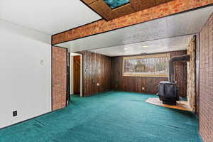 Unfurnished living room featuring a wood stove, wood walls, carpet floors, and brick wall