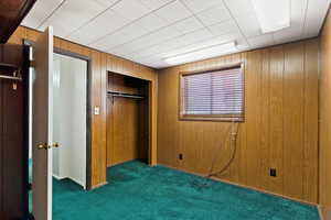 Unfurnished bedroom featuring dark colored carpet, wooden walls, and a closet