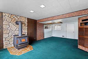 Unfurnished living room with a wood stove, wood walls, and dark carpet