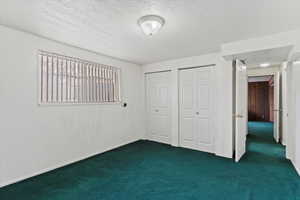 Unfurnished bedroom featuring multiple closets, dark carpet, and a textured ceiling