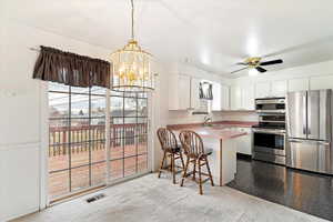 Kitchen with kitchen peninsula, appliances with stainless steel finishes, sink, white cabinetry, and a breakfast bar area