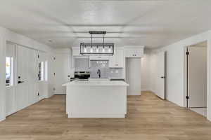 Kitchen with stainless steel range with electric cooktop, white cabinets, hanging light fixtures, light wood-type flooring, and a kitchen island