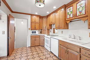 Kitchen featuring decorative backsplash, ornamental molding, white appliances, sink, and decorative light fixtures