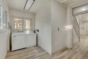 Clothes washing area with brick wall, light hardwood / wood-style flooring, and washing machine and clothes dryer