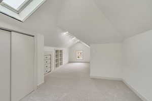 Bonus room with vaulted ceiling with skylight, built in shelves, and light carpet