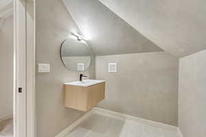 Bathroom with tile patterned floors, vanity, and vaulted ceiling