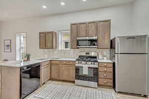 Kitchen featuring sink, light wood-type flooring, tasteful backsplash, kitchen peninsula, and stainless steel appliances