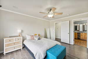 Bedroom with ensuite bath, ceiling fan, dark hardwood / wood-style flooring, and crown molding