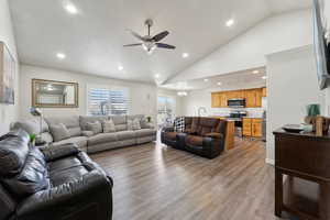 Living room with ceiling fan with notable chandelier, light wood-type flooring, high vaulted ceiling, and sink