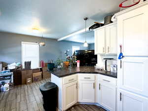 Kitchen featuring white cabinetry, kitchen peninsula, pendant lighting, a textured ceiling, and wood-type flooring