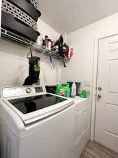 Clothes washing area featuring a textured ceiling, light hardwood / wood-style flooring, and washer and clothes dryer