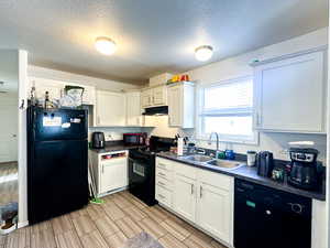 Kitchen featuring sink, white cabinets, black appliances, and a textured ceiling