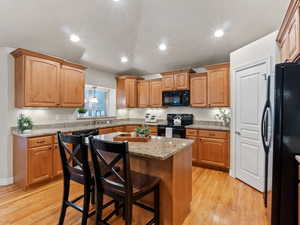 Kitchen featuring black appliances, a kitchen breakfast bar, a kitchen island, and light wood-type flooring