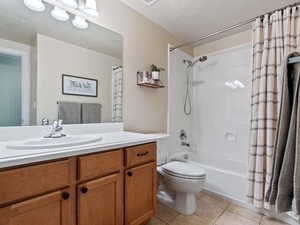 Full bathroom featuring shower / bath combination with curtain, vanity, a textured ceiling, tile patterned flooring, and toilet