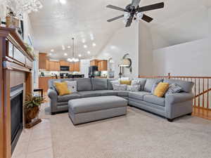 Living room featuring high vaulted ceiling, a textured ceiling, a fireplace, light tile patterned flooring, and ceiling fan with notable chandelier