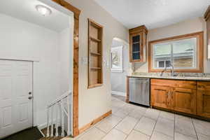 Kitchen with light stone counters, a textured ceiling, sink, dishwasher, and light tile patterned flooring