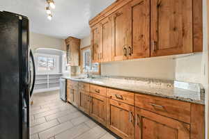 Kitchen with light stone countertops, black fridge, stainless steel dishwasher, and a textured ceiling