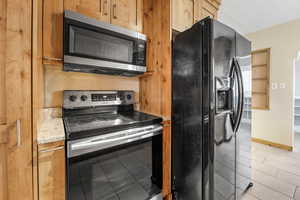 Kitchen featuring appliances with stainless steel finishes, a textured ceiling, light tile patterned floors, and light stone counters