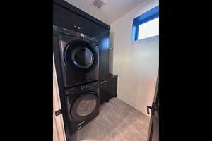 Washroom featuring stacked washer and dryer and cabinets