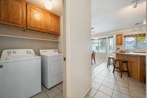 Clothes washing area with sink, cabinets, a textured ceiling, washer and clothes dryer, and light tile patterned flooring