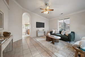 Tiled living room featuring lofted ceiling, ceiling fan, and crown molding