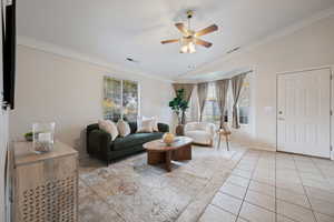 Living room featuring ceiling fan, light tile patterned floors, crown molding, and vaulted ceiling