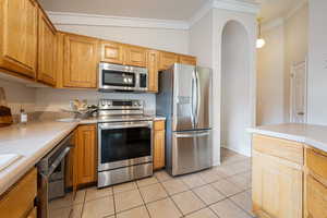 Kitchen with hanging light fixtures, vaulted ceiling, ornamental molding, light tile patterned floors, and stainless steel appliances