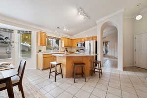 Kitchen with rail lighting, a kitchen island, vaulted ceiling, light tile patterned floors, and appliances with stainless steel finishes